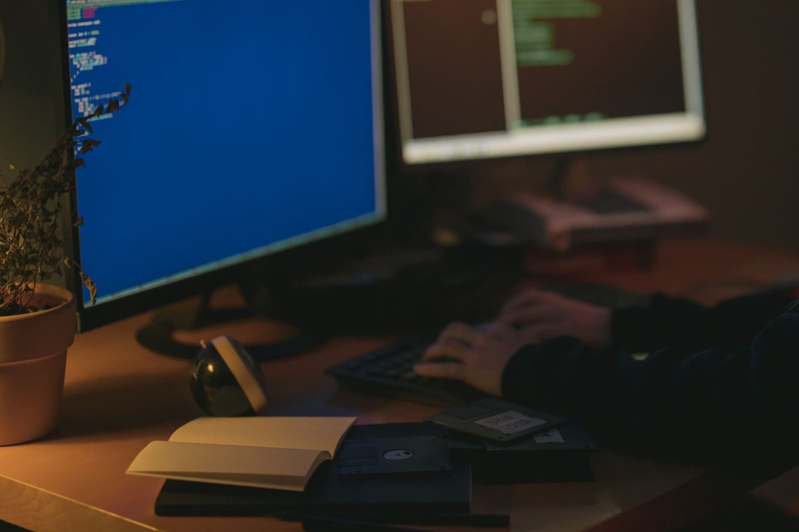 Manos programando frente a dos monitores con código en un espacio en penumbra